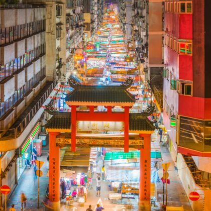 The highrise apartment buildings of Kowloon overlooking the crowded stalls of Temple Street Night Market and traditional Chinese entrance gate in Hong Kong.